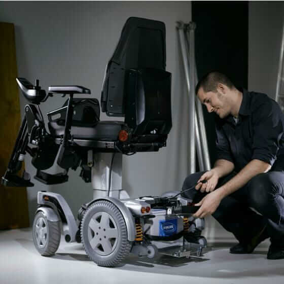 Tecnico che lavora su una carrozzina elettrica per mobilità autonoma, evidenziando la manutenzione delle carrozzine elettriche per mobilità autonoma.